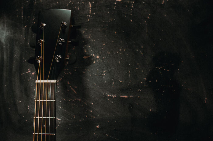 acoustic-guitar-stands-against-wall-against-dark-background